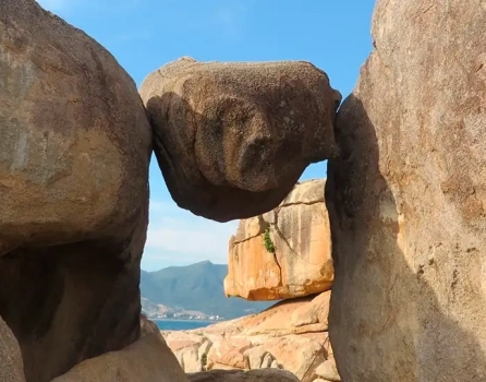 Балансирующий камень между скалами в Саду камней Хон Чонг, Нячанг — вид на море и горы
