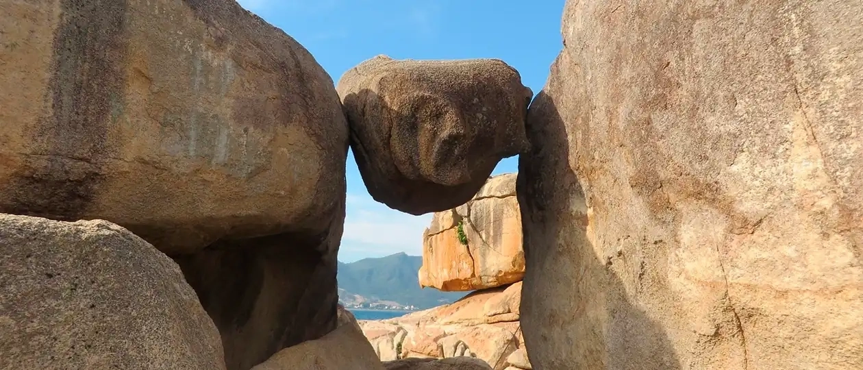 Балансирующий камень между скалами в Саду камней Хон Чонг, Нячанг — вид на море и горы