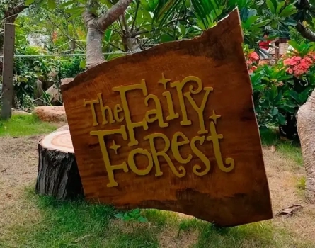 Деревянная табличка с надписью The Fairy Forest среди деревьев и зелени